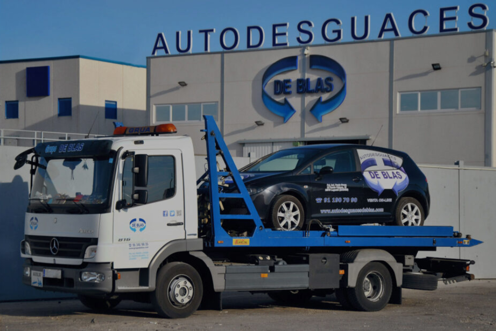 Grúa con coche para llevar a Autodesguaces de Blas, con letrero de fondo